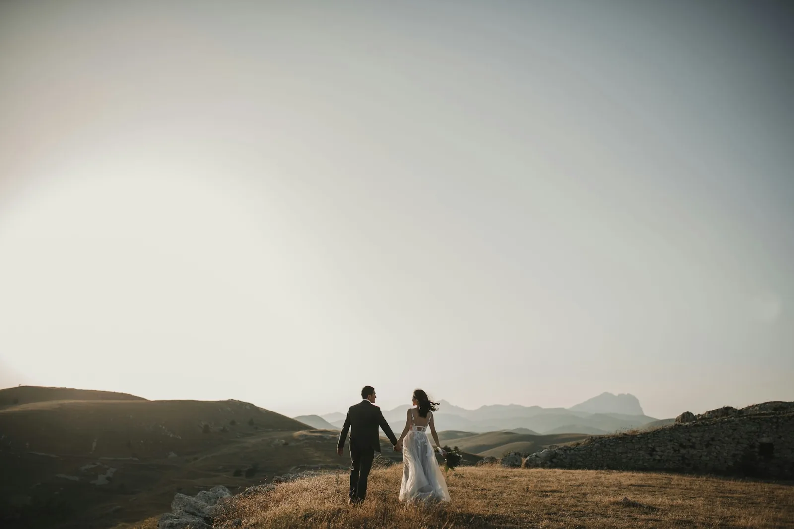 Pareja de novios caminando por una loma al atardecer